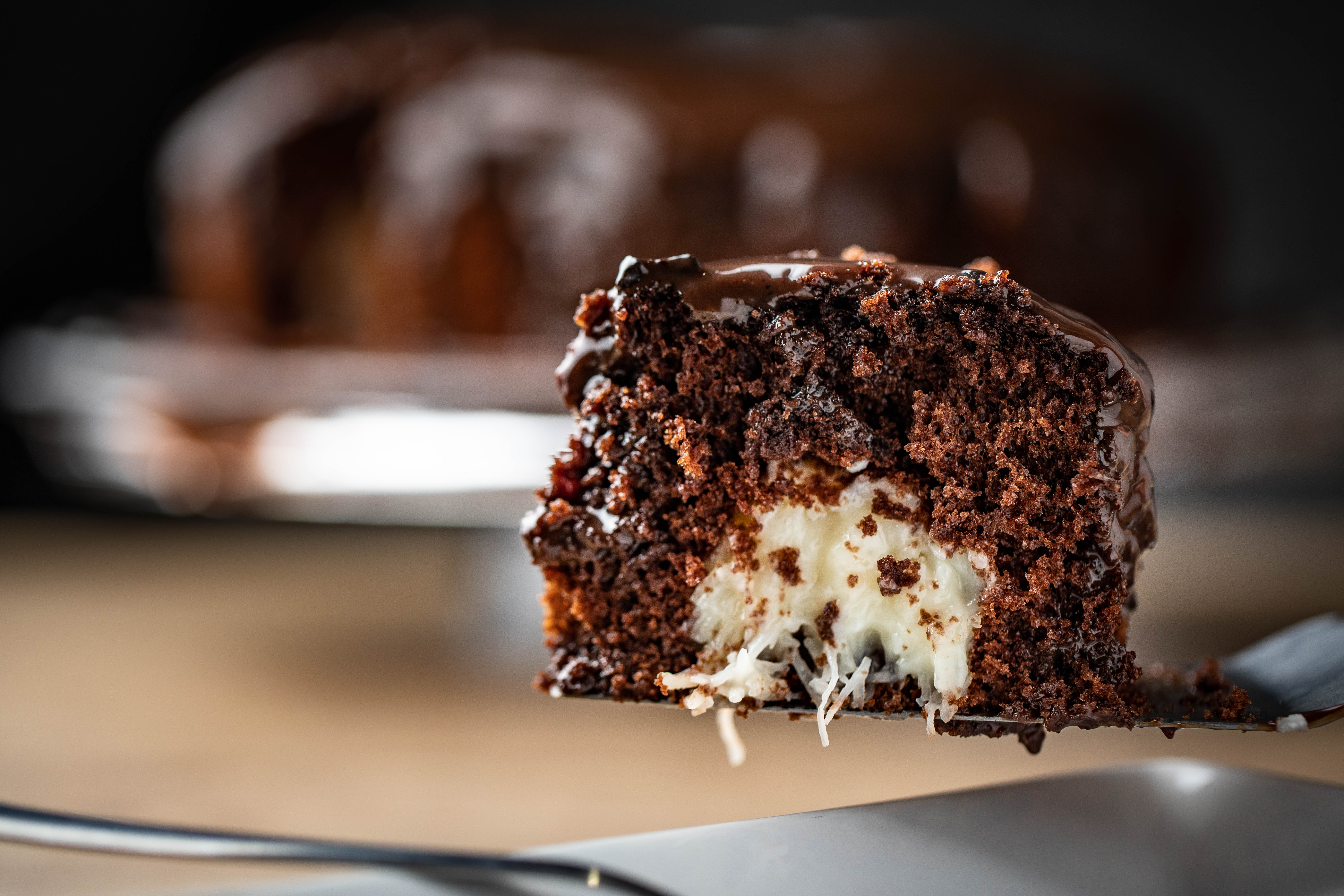 Pedaço de bolo de chocolate com recheio de cocada no centro e cobertura de brigadeiro sobre espátula e prato branco.